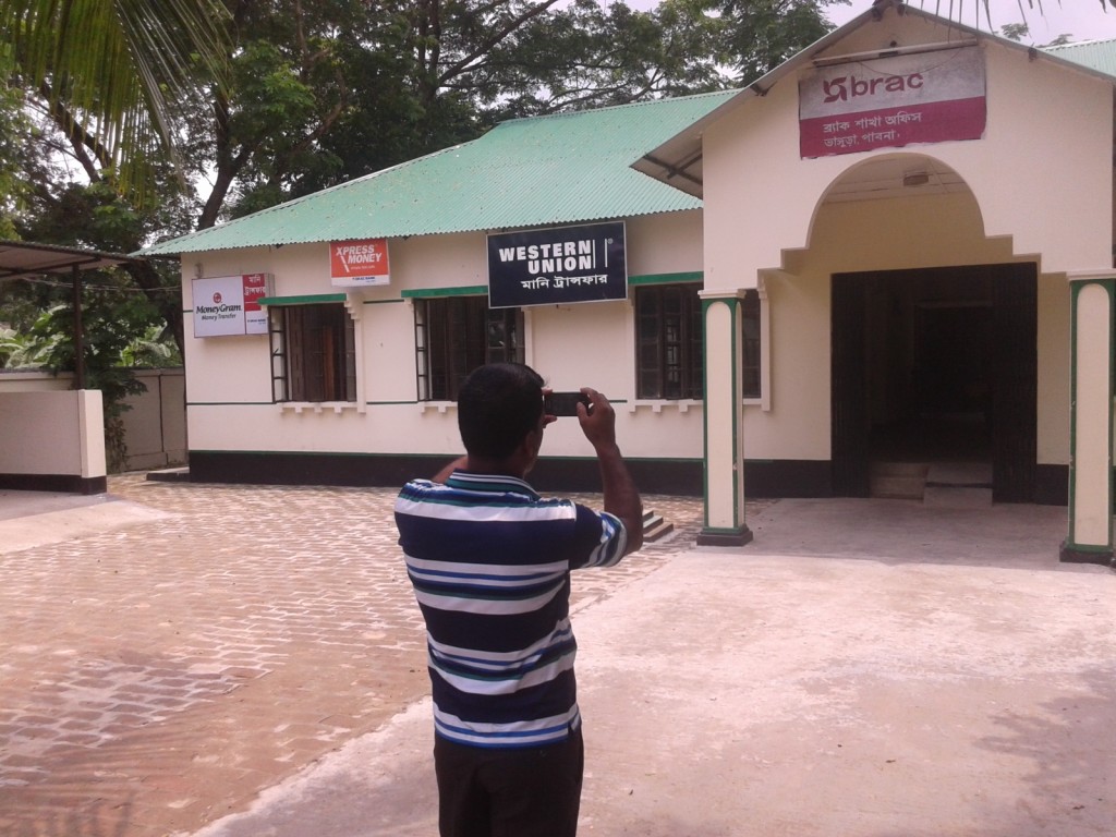 Enumerator taking a photograph of a BRAC building 